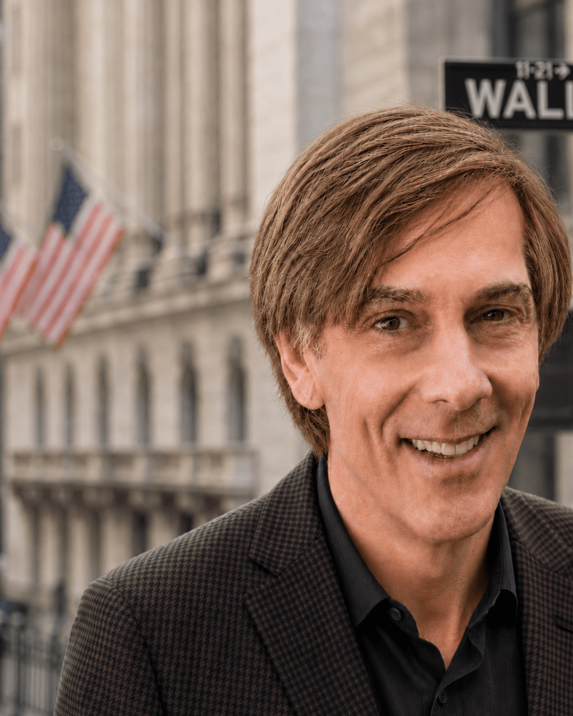 Smiling man in suit near Wall Street sign